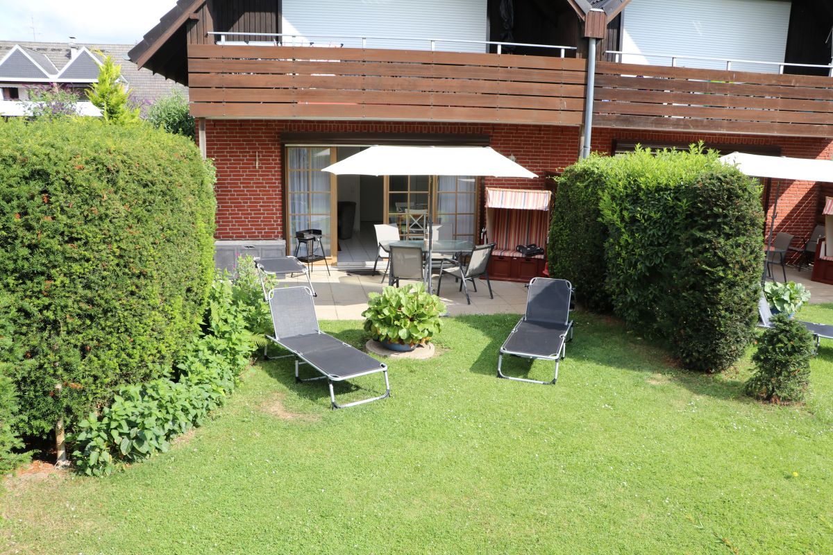 Terrasse und Garten von Haus Henning mit Sonnenschirm, Tischgruppe und Sonnenliegen.